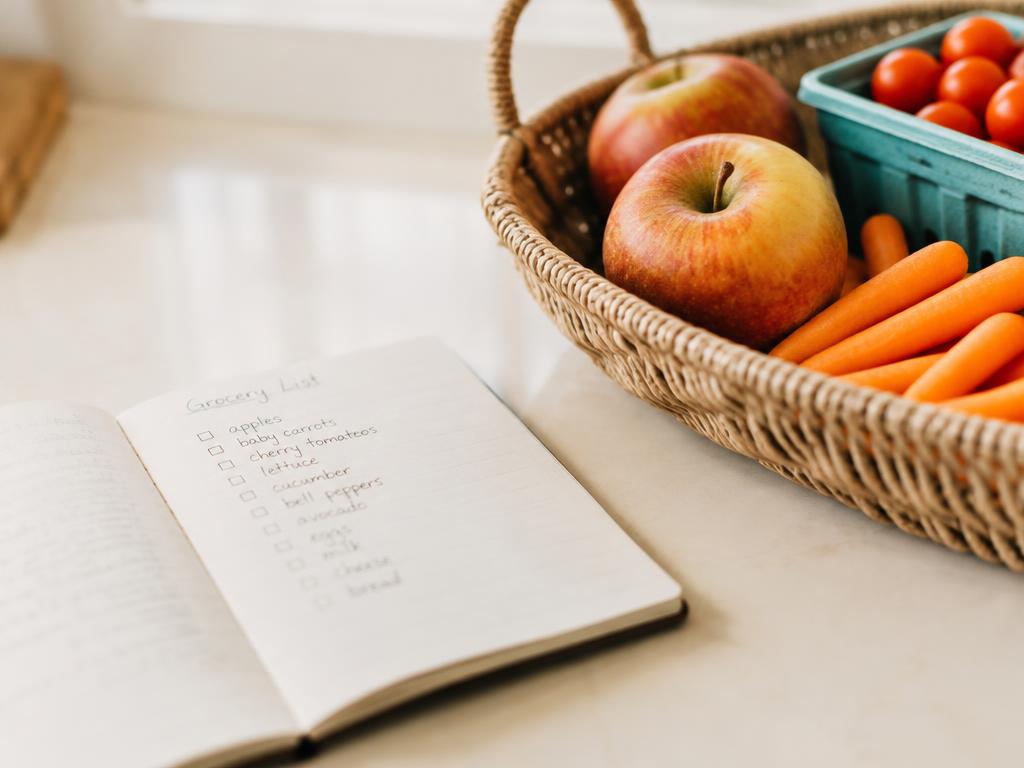 Cuaderno con la lista de compras por categorías junto a una canasta con frutas y verduras